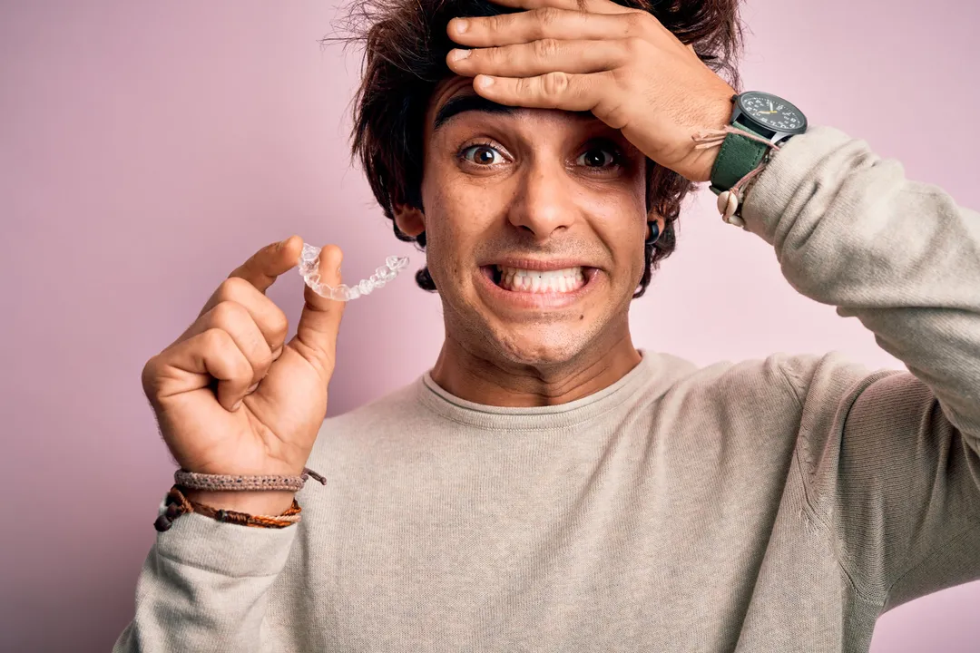 A man grimacing while holding a mail-order clear aligner