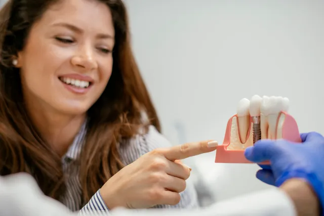 A smiling patient pointing at a dental implant model held by a dentist